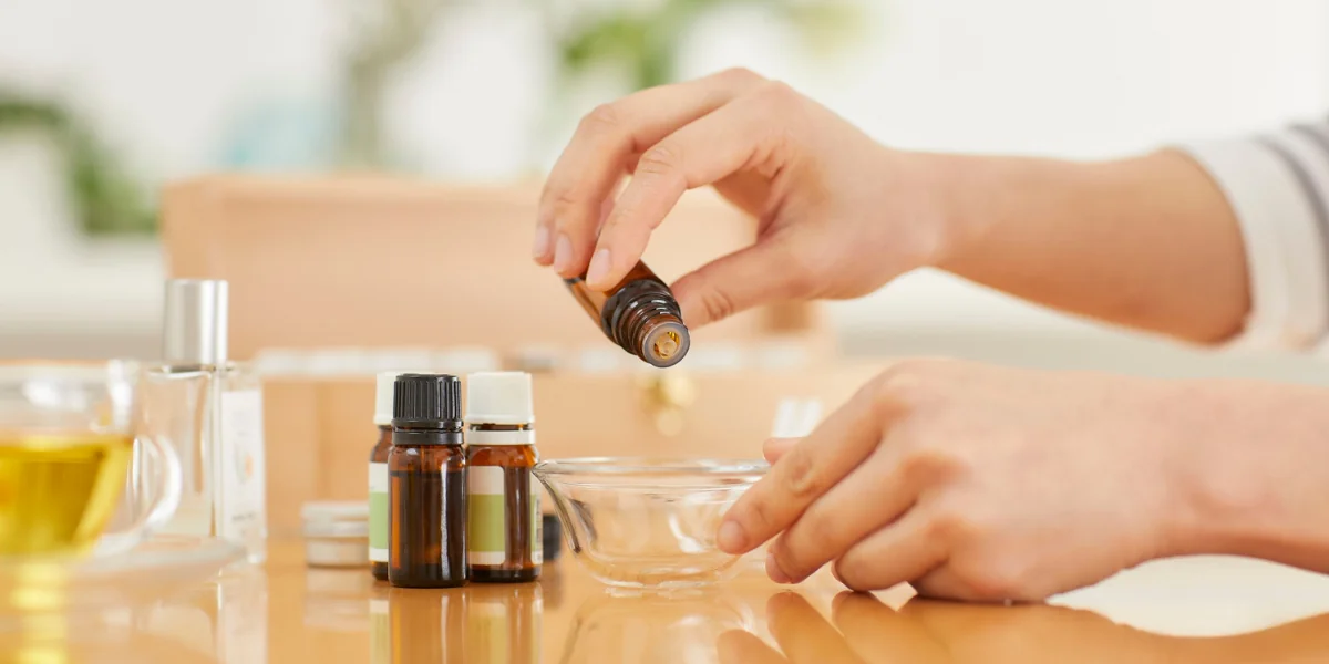 Hand dropping essential oil into a small bowl with other essential oil bottles on the table.