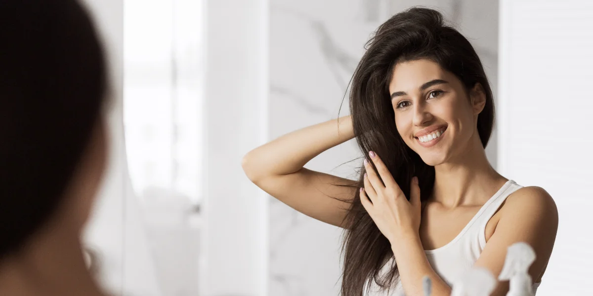 Woman smiling while looking at herself in the mirror as she’s fixing her hair