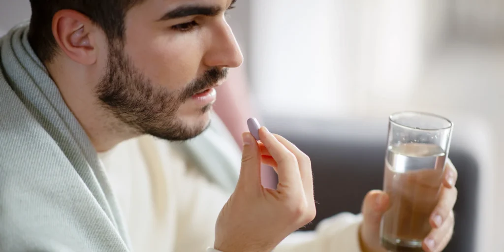 Man taking oral finasteride tablet with water as part of hair loss treatment routine